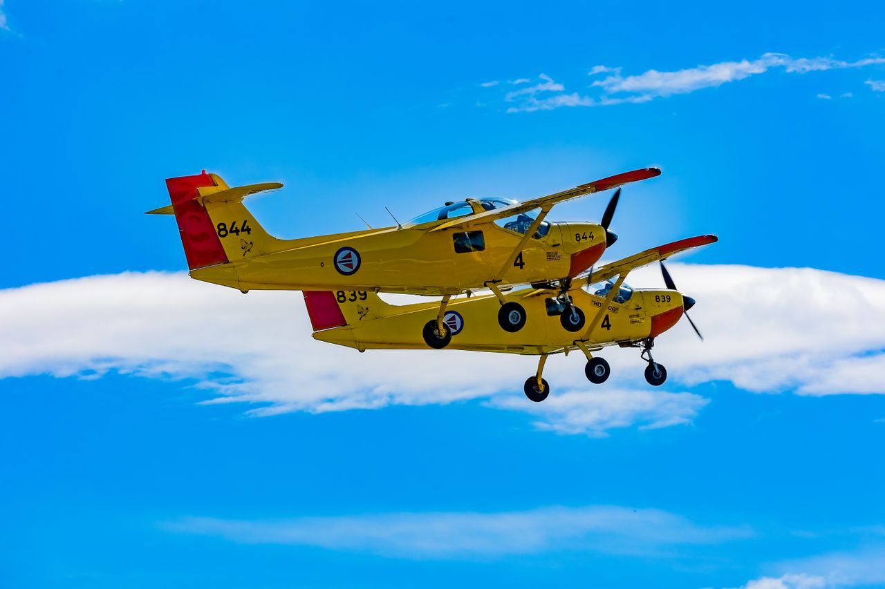 Two vintage yellow aircraft performing a precise aerial maneuver against a clear blue sky.